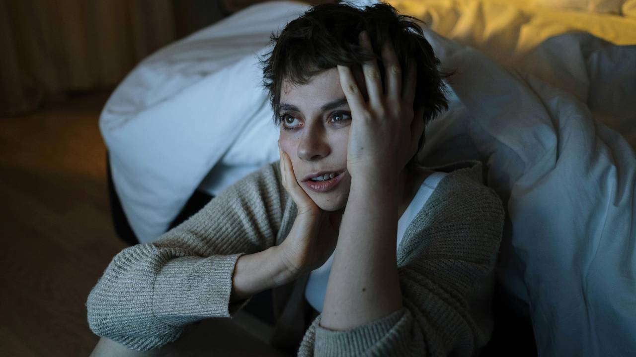 zena umorna od nesanice, sedi pored kreveta